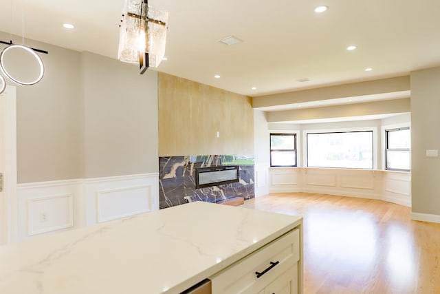 kitchen with a decorative wall, light stone countertops, recessed lighting, a wainscoted wall, and light wood-type flooring