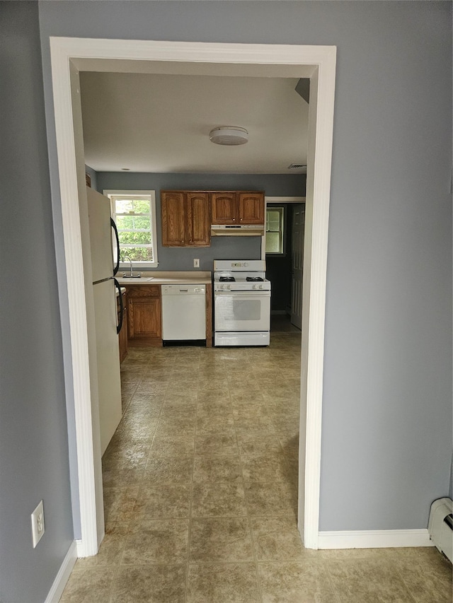 kitchen with white appliances, under cabinet range hood, a sink, brown cabinetry, and baseboard heating