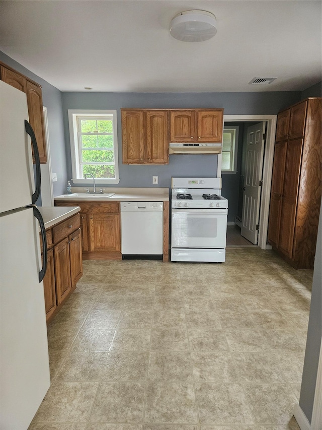 kitchen with white appliances, a sink, light countertops, and brown cabinets