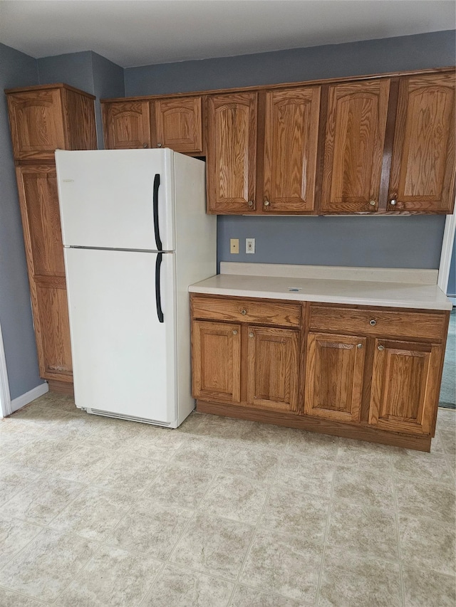 kitchen featuring freestanding refrigerator, brown cabinets, and light countertops