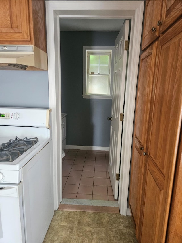 kitchen featuring range hood, white gas range, brown cabinets, and light tile patterned floors