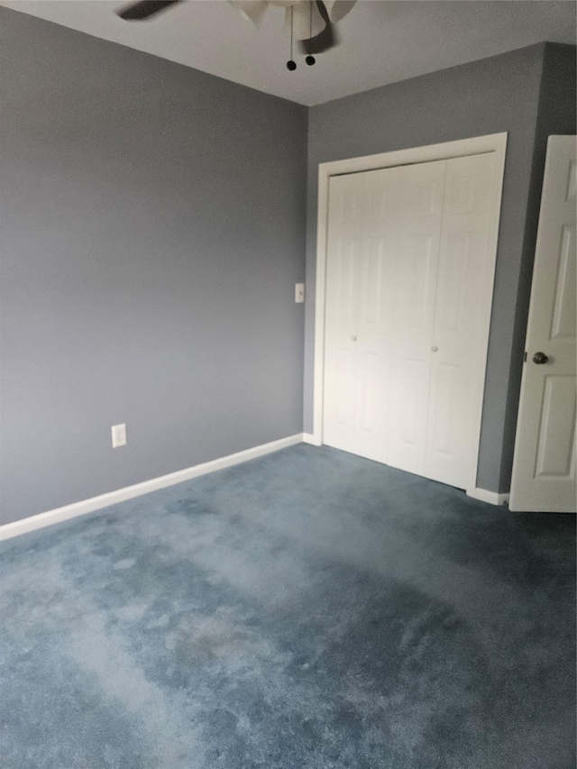 unfurnished bedroom with dark carpet, baseboards, a closet, and a ceiling fan
