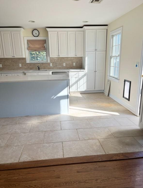 kitchen featuring light countertops, backsplash, white cabinets, a sink, and baseboards