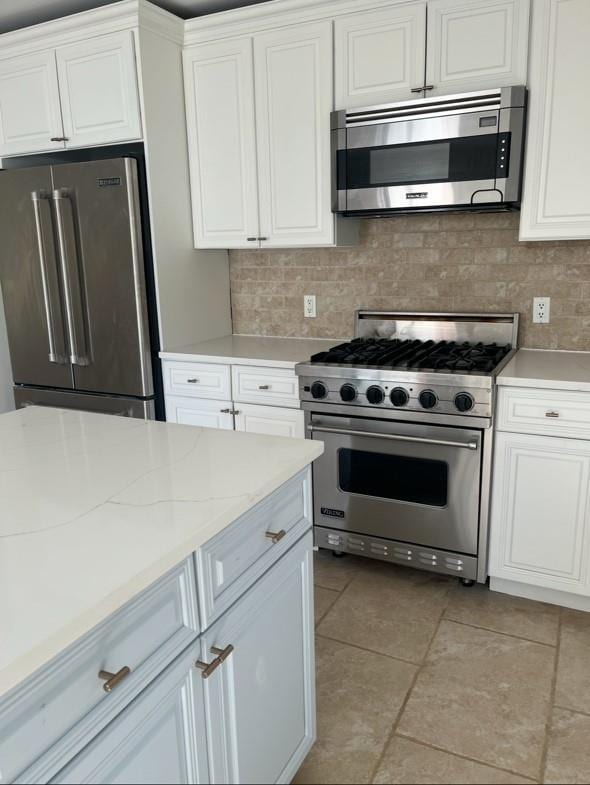 kitchen featuring high quality appliances, white cabinets, tasteful backsplash, light tile patterned flooring, and light stone counters
