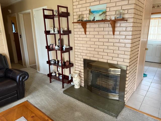 living area with a brick fireplace, carpet flooring, and tile patterned floors