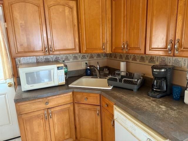 kitchen with white appliances, a sink, brown cabinetry, and dark countertops