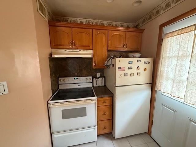 kitchen featuring white appliances, under cabinet range hood, brown cabinetry, and light tile patterned floors