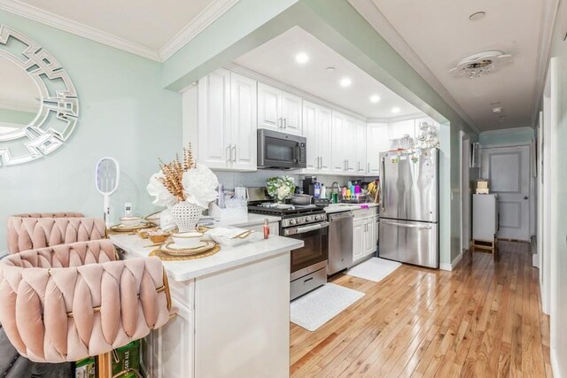 23118 145th Ave, Springfield Gardens, NY 11413 - kitchen featuring stainless steel appliances, white cabinetry, ornamental molding, a peninsula, and light wood finished floors