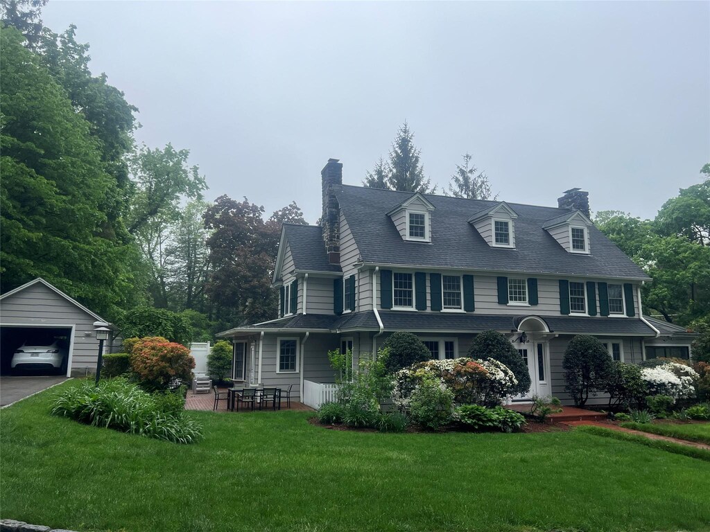 view of front of house with a detached garage, a chimney, an outdoor structure, a front yard, and driveway