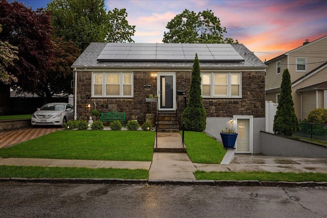 view of front facade with stone siding, a yard, solar panels, and roof with shingles