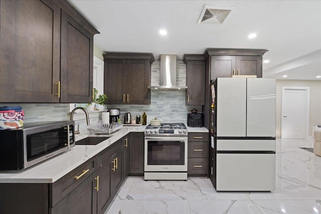 kitchen featuring stainless steel appliances, wall chimney exhaust hood, a sink, light marble finish floors, and dark brown cabinetry