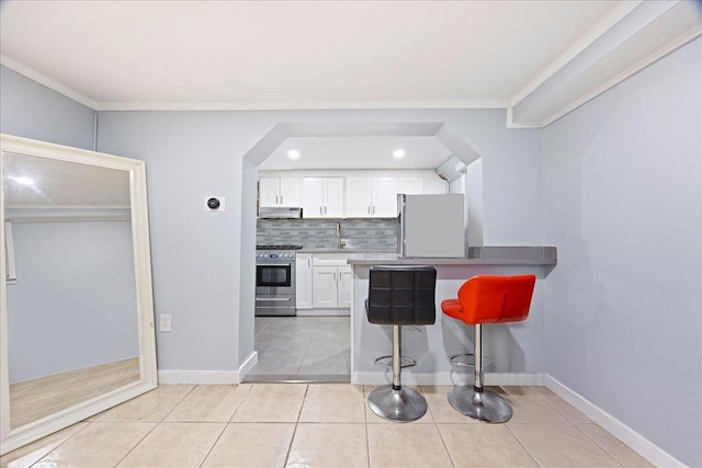 kitchen with appliances with stainless steel finishes, a kitchen bar, under cabinet range hood, crown molding, and white cabinetry