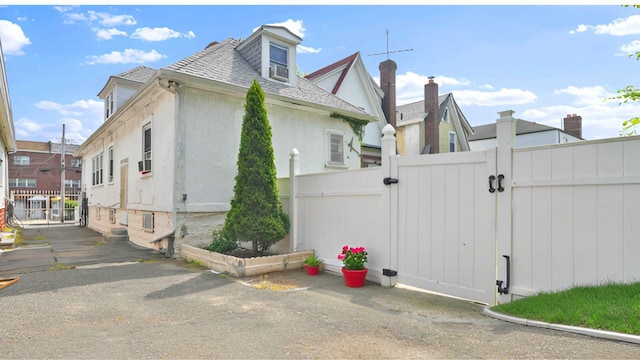 view of property exterior with a gate, fence, stucco siding, and roof with shingles