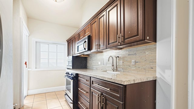 kitchen featuring stainless steel microwave, a sink, decorative backsplash, light tile patterned floors, and dark brown cabinets
