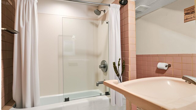 full bath featuring shower / bath combo, tile walls, a sink, and wainscoting