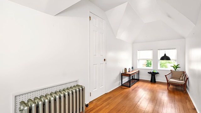 sitting room with radiator heating unit, wood-type flooring, vaulted ceiling, and baseboards