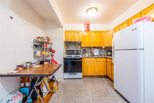 kitchen with freestanding refrigerator, gas range, granite tiled floors, decorative backsplash, and a sink