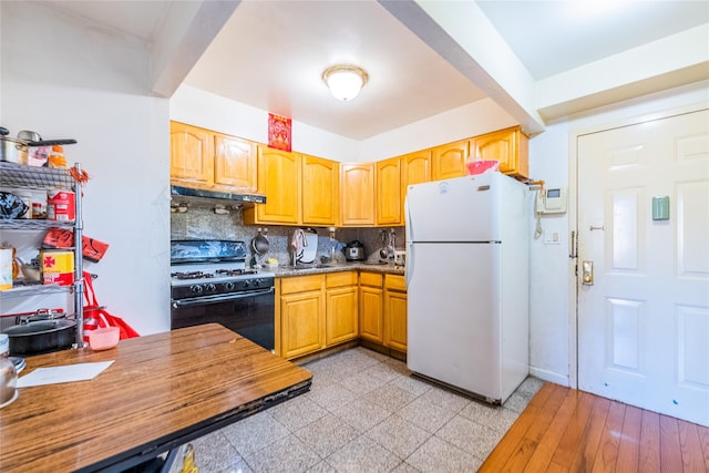 kitchen with freestanding refrigerator, gas stove, under cabinet range hood, backsplash, and a sink