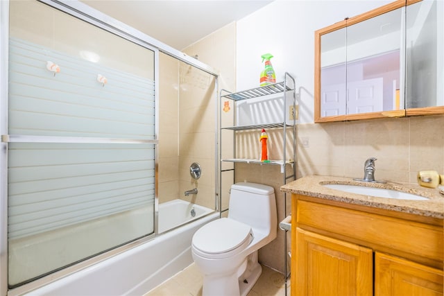 bathroom featuring toilet, shower / bath combination with glass door, vanity, tile walls, and tile patterned floors