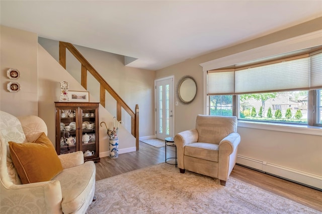 living area with wood finished floors, stairs, a baseboard heating unit, and baseboards