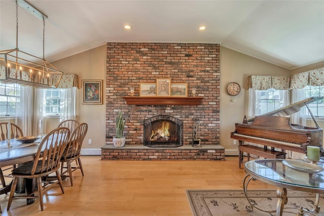 living area featuring vaulted ceiling, a brick fireplace, wood finished floors, baseboards, and a chandelier