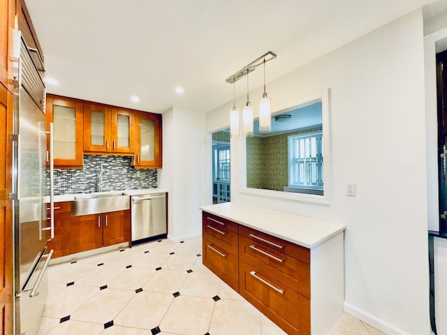 kitchen with appliances with stainless steel finishes, a sink, brown cabinets, tasteful backsplash, and glass insert cabinets