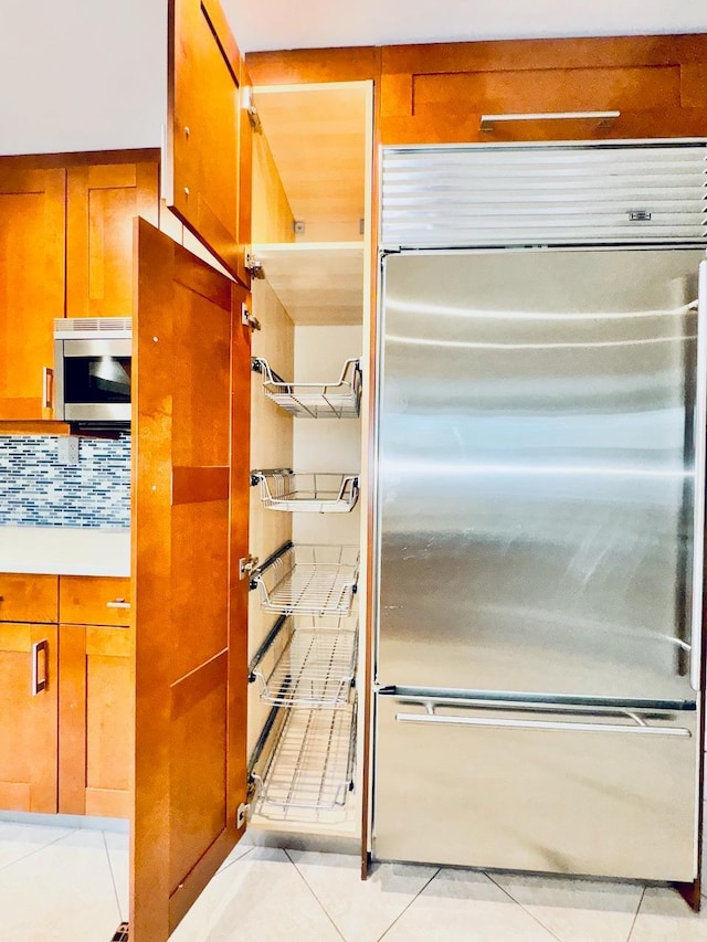 kitchen with appliances with stainless steel finishes, light tile patterned floors, brown cabinets, and backsplash
