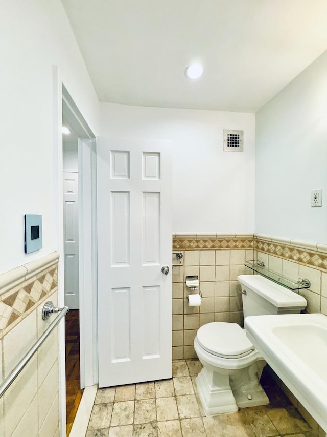 bathroom featuring tile walls, toilet, a wainscoted wall, recessed lighting, and a sink