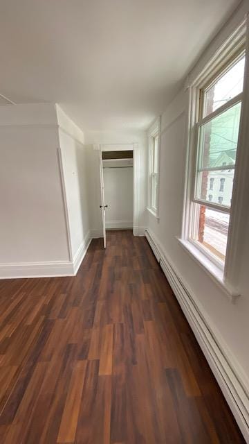 hallway with baseboard heating, plenty of natural light, dark wood-type flooring, and baseboards