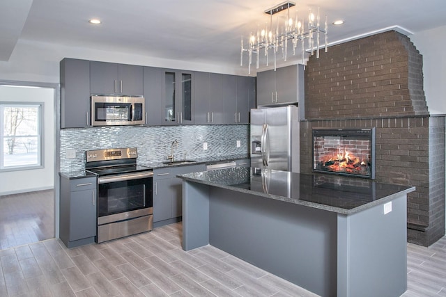 kitchen featuring appliances with stainless steel finishes, gray cabinets, a sink, a chandelier, and light wood-style flooring