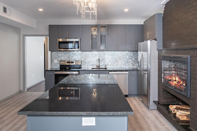 kitchen featuring stainless steel appliances, a sink, a center island, tasteful backsplash, and light wood-style flooring