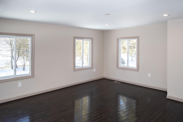 empty room featuring healthy amount of natural light, dark wood finished floors, baseboards, and recessed lighting
