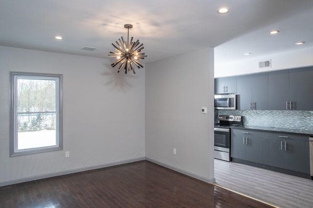 kitchen with appliances with stainless steel finishes, wood finished floors, a chandelier, tasteful backsplash, and recessed lighting