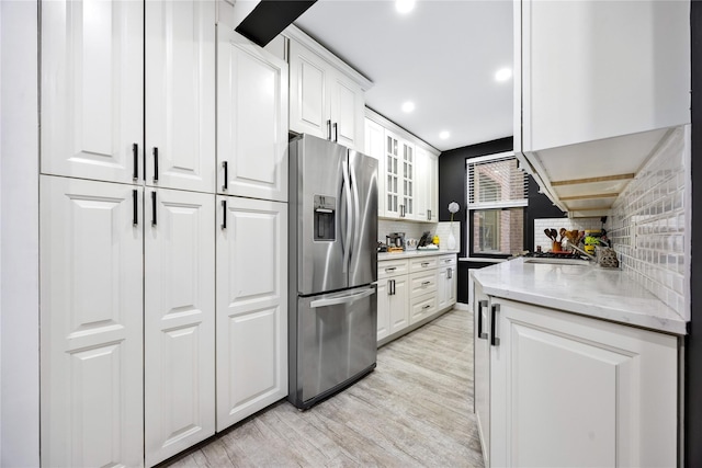kitchen featuring stainless steel fridge with ice dispenser, decorative backsplash, light wood-style floors, white cabinetry, and light stone countertops