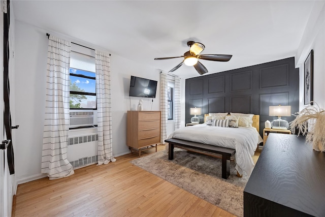 bedroom with radiator heating unit, multiple windows, light wood-style flooring, ceiling fan, and a decorative wall