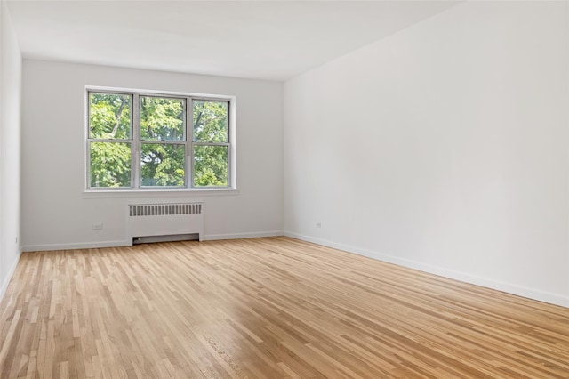 empty room featuring radiator, light wood-style flooring, and baseboards