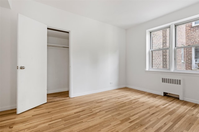 unfurnished bedroom featuring radiator, light wood-type flooring, and baseboards