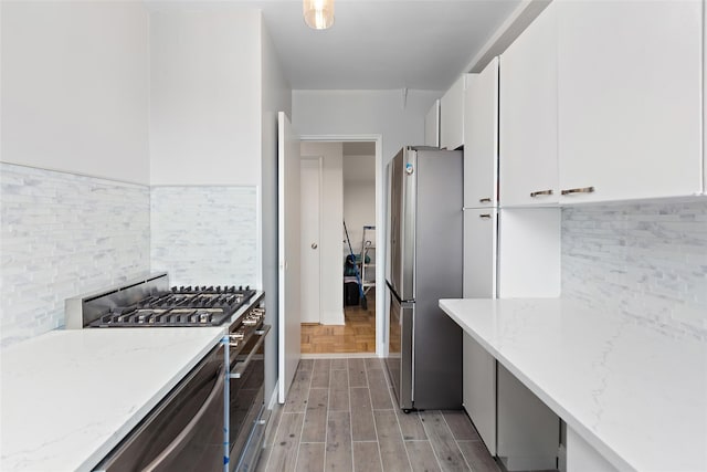 5500 Fieldston Rd Unit 77, Bronx, NY 10471 - kitchen featuring stainless steel appliances, white cabinets, tasteful backsplash, light stone countertops, and light wood-style floors