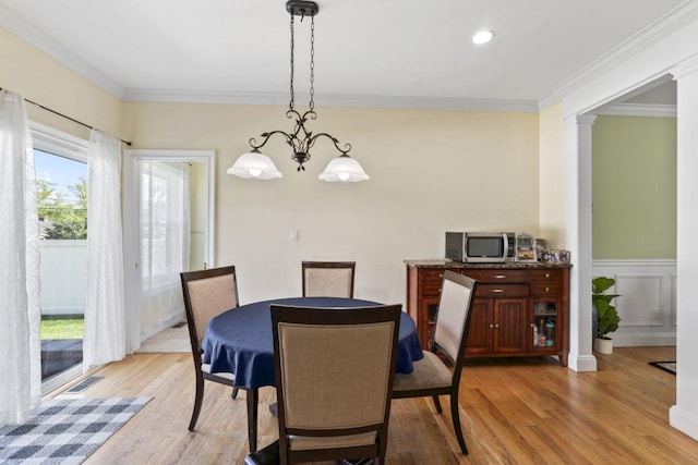 dining area featuring light wood finished floors, crown molding, a chandelier, and wainscoting