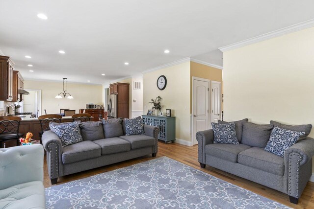 living room featuring ornamental molding, light wood-style flooring, recessed lighting, baseboards, and a chandelier