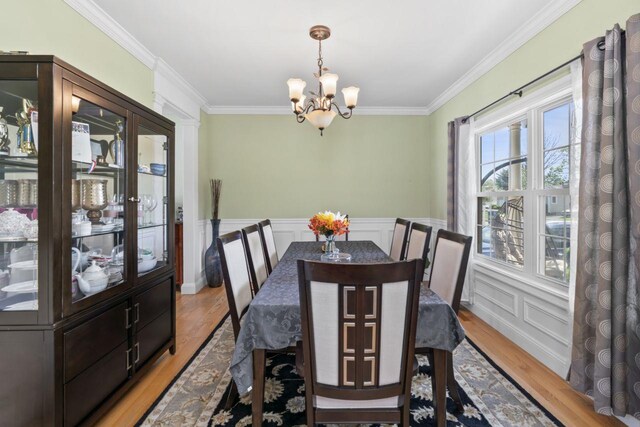 dining area featuring a chandelier, light wood finished floors, ornamental molding, a decorative wall, and wainscoting
