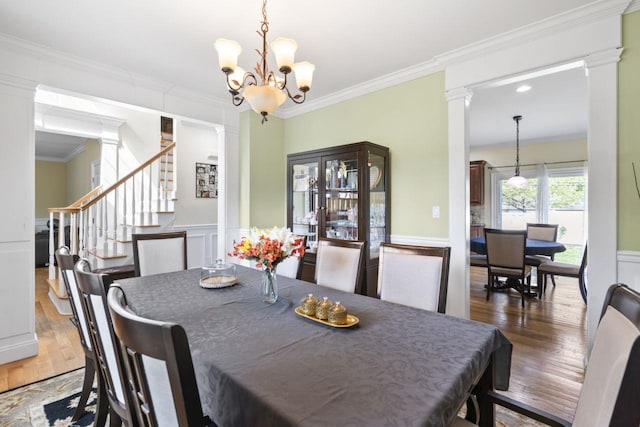 dining space featuring decorative columns, ornamental molding, a chandelier, wood finished floors, and stairway