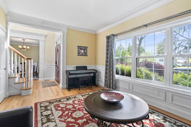 sitting room with plenty of natural light, wood finished floors, ornate columns, a decorative wall, and ornamental molding