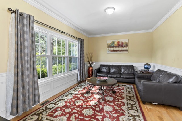 living area featuring crown molding, wood finished floors, wainscoting, and a decorative wall