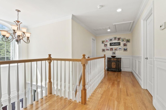 hall with attic access, an upstairs landing, light wood finished floors, a chandelier, and crown molding
