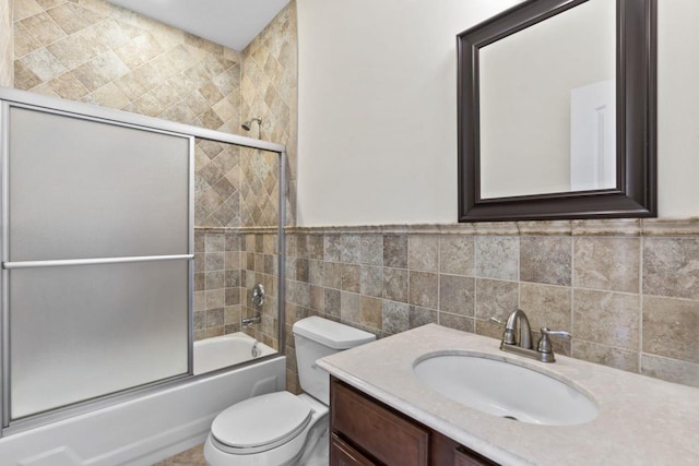full bath with tile walls, bath / shower combo with glass door, toilet, and vanity