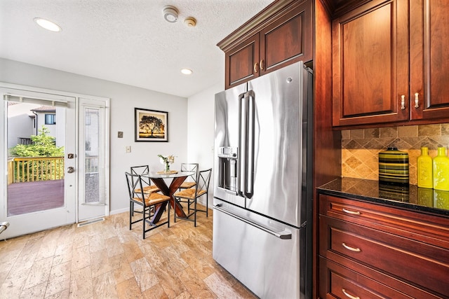 kitchen featuring stainless steel fridge with ice dispenser, backsplash, recessed lighting, dark stone counters, and a textured ceiling