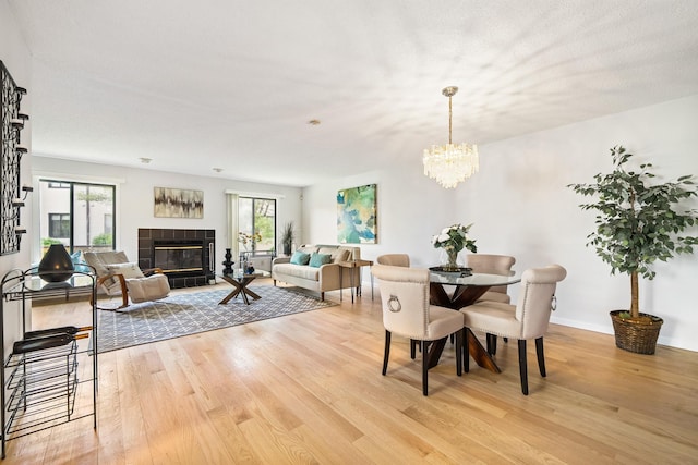 dining area featuring light wood finished floors, healthy amount of natural light, a chandelier, and a tile fireplace