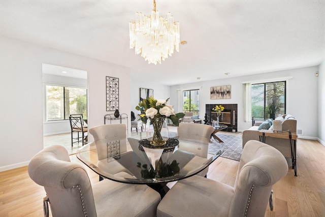 dining room featuring a chandelier, light wood-style flooring, baseboards, and a tiled fireplace
