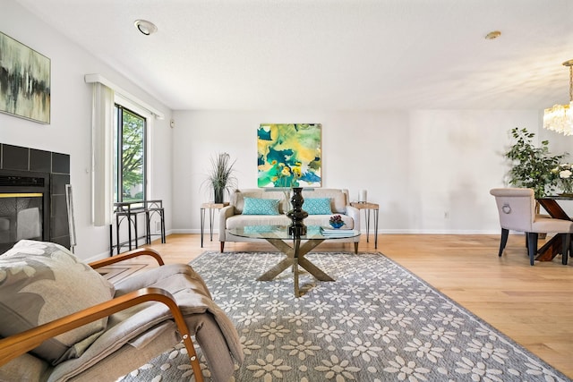 living area with a chandelier, wood finished floors, baseboards, and a tile fireplace